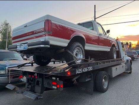 A red ford truck is being towed by a tow truck.