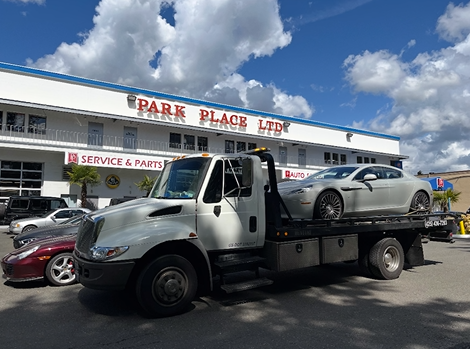 A tow truck with two cars on the back is parked in front of a building.