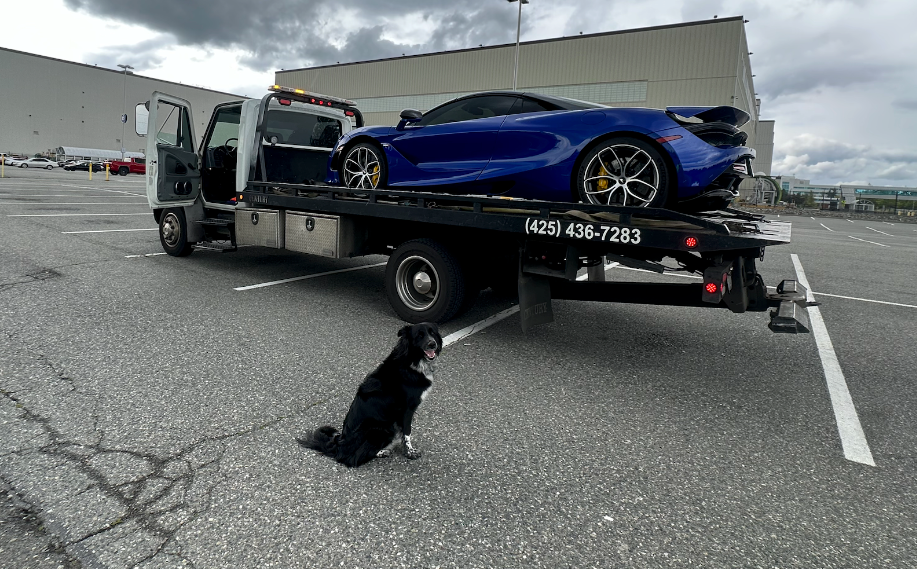 A tow truck is towing a blue sports car in a parking lot.