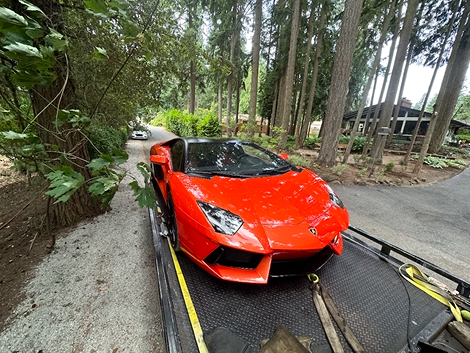 A red lamborghini aventador is being towed down a road.
