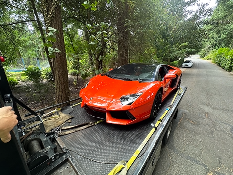 A red lamborghini aventador is sitting on top of a tow truck.