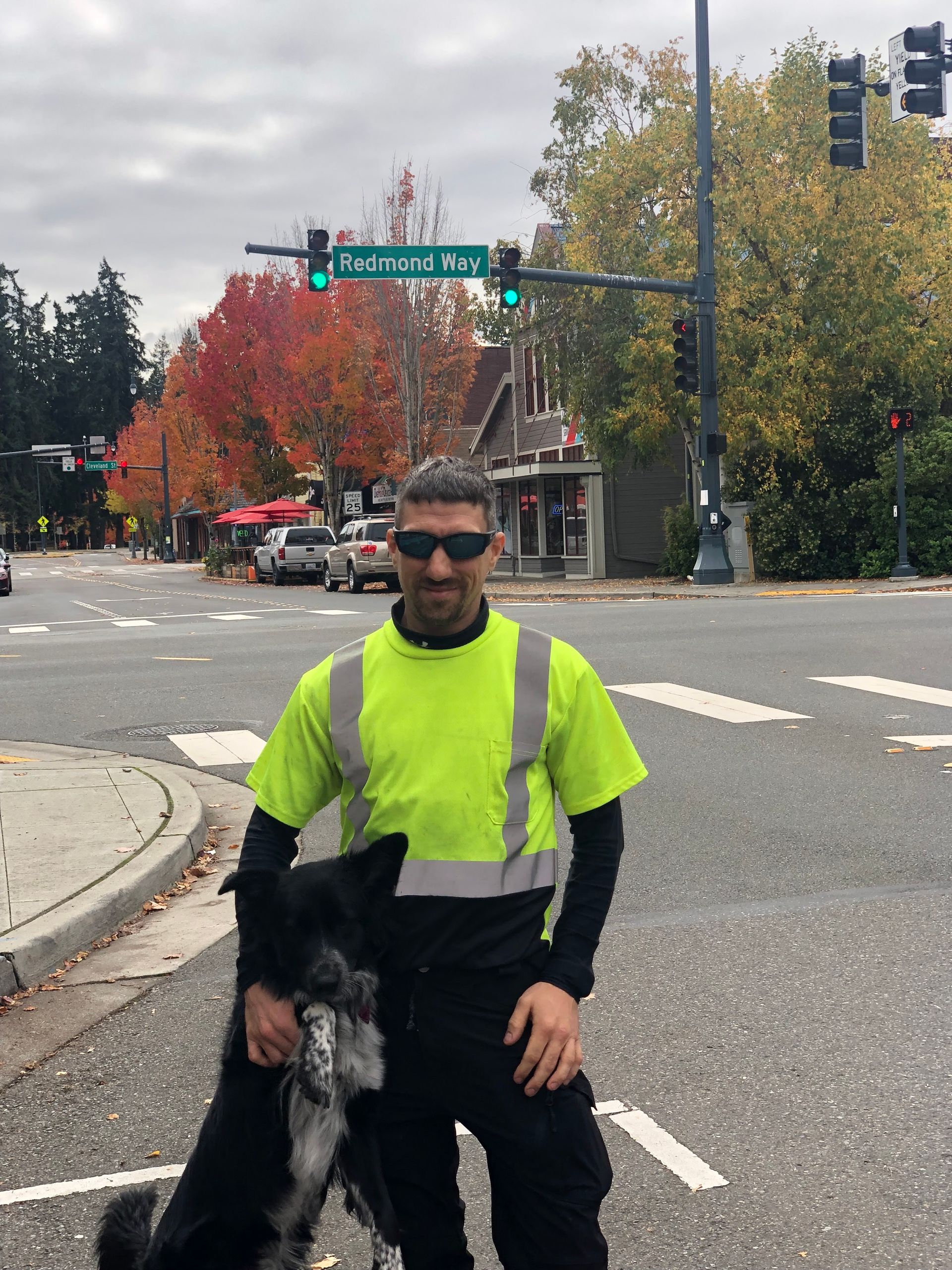A man in a yellow safety vest stands next to a black dog