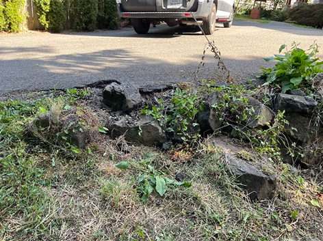 A car is parked in a driveway next to a rock wall.