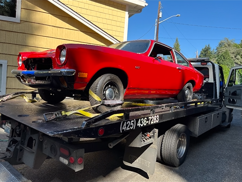 A red car is sitting on top of a tow truck.