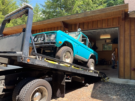 A blue truck is being towed to a garage by a tow truck.