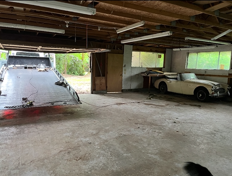 A white car is parked in a garage next to a tow truck.