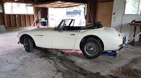 A white sports car is parked in a garage on a jack.