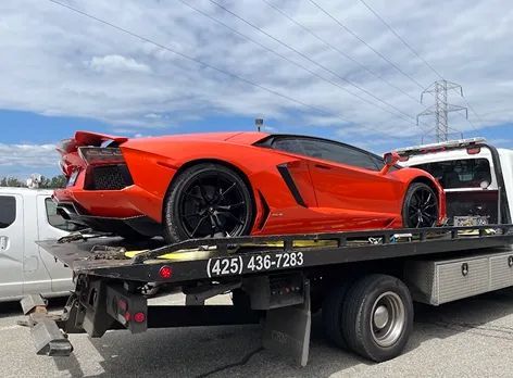 Orange Lamborghini loaded on a tow truck, with phone number on truck.