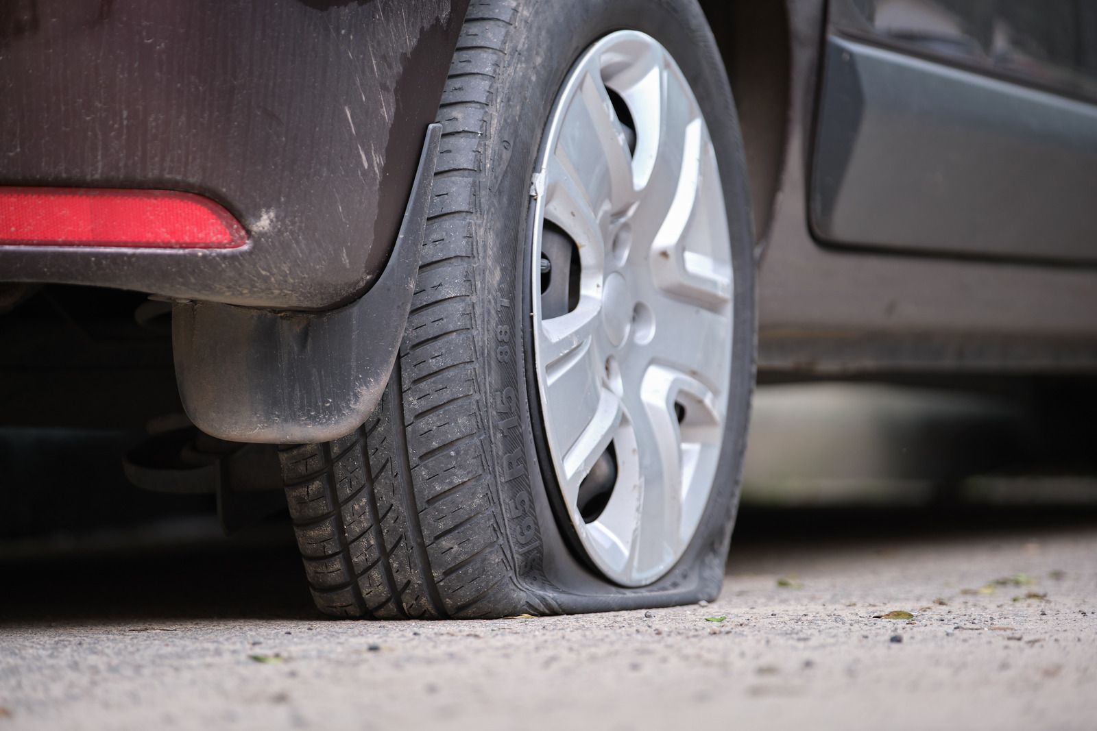 Flat tire on a car; close up view. Gray tire is deflated, resting on pavement. Black car.