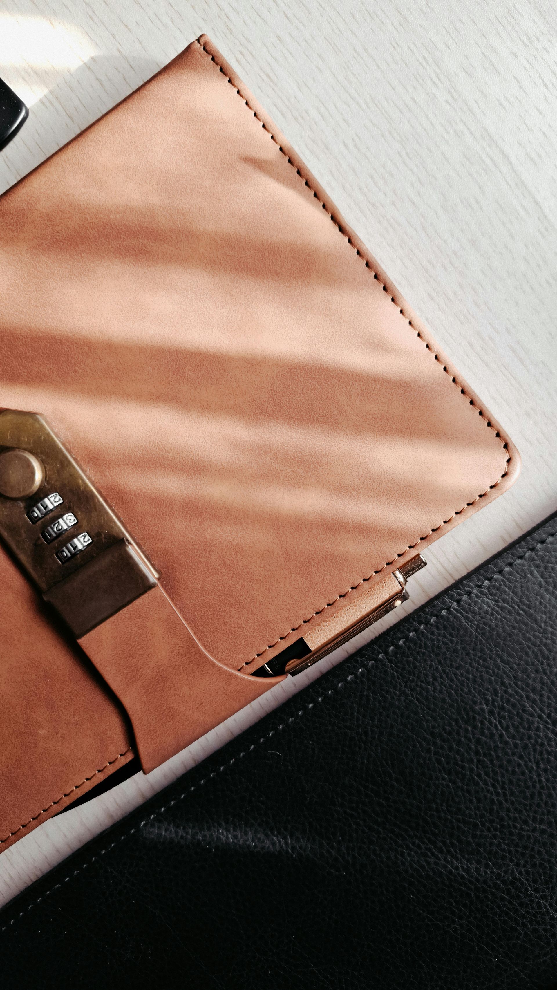 Un cuaderno de gamuza marrón claro con cierre de combinación metálico, que reposa junto a una superficie negra texturizada.