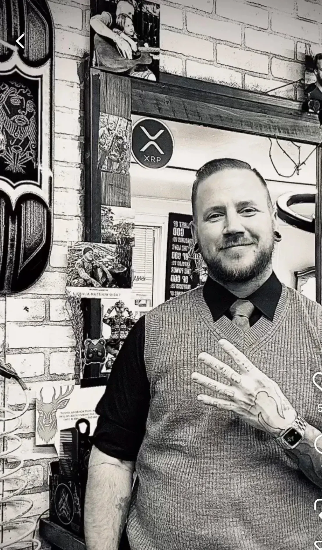 A smiling person in a sweater vest and collared shirt holds up four fingers in front of a brick wall and a framed mirror.