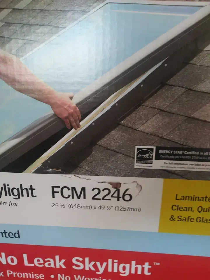 A hand holding a skylight over a shingled roof. Text reads 