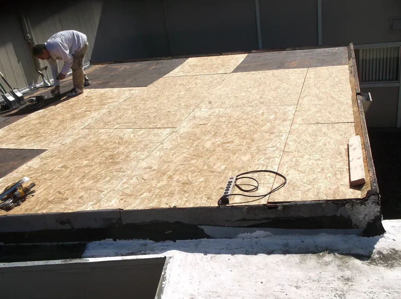 Person working on a rooftop, laying wood panels for a new roof. Sunlight.