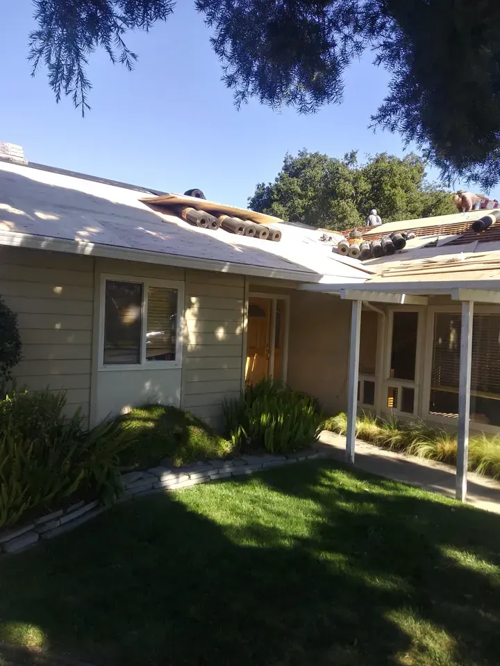 House with roof partially stripped, ready for re-roofing; green grass, bright sky.