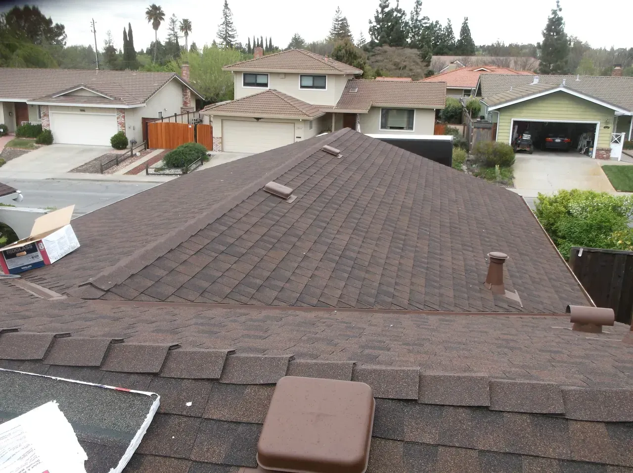 Brown asphalt shingle roof on a house, view of other houses in a suburban neighborhood.