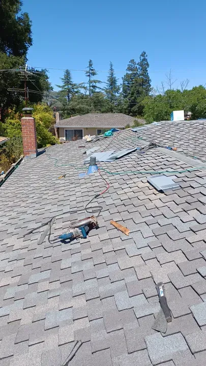 Rooftop with asphalt shingles under clear blue sky, tools, and a brick chimney.