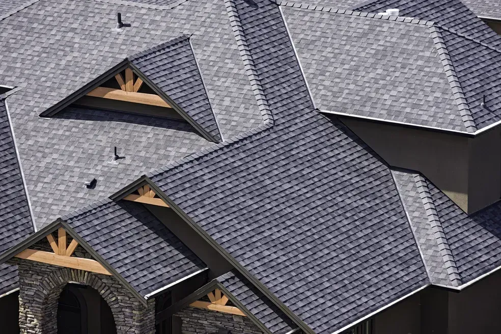 Gray shingled roof of a house with multiple peaks and gables. Wooden supports visible under the eaves.