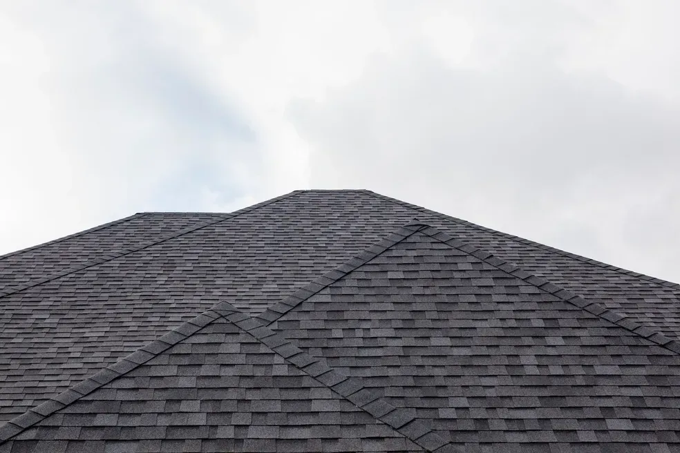 Gray asphalt shingle roof against a cloudy sky.