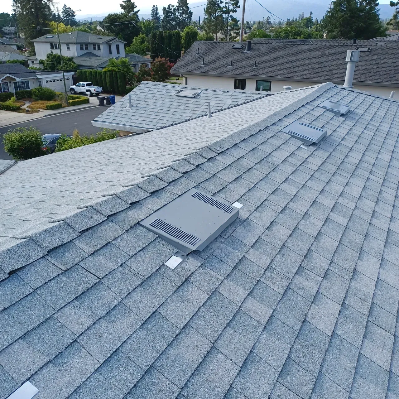 Gray shingle roof with three rectangular vents, overlooking residential neighborhood.