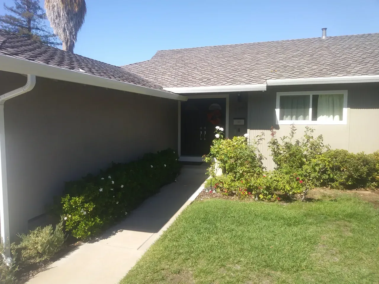 Exterior of a house with a gray roof and siding, green lawn, bushes, and a pathway to the front door.