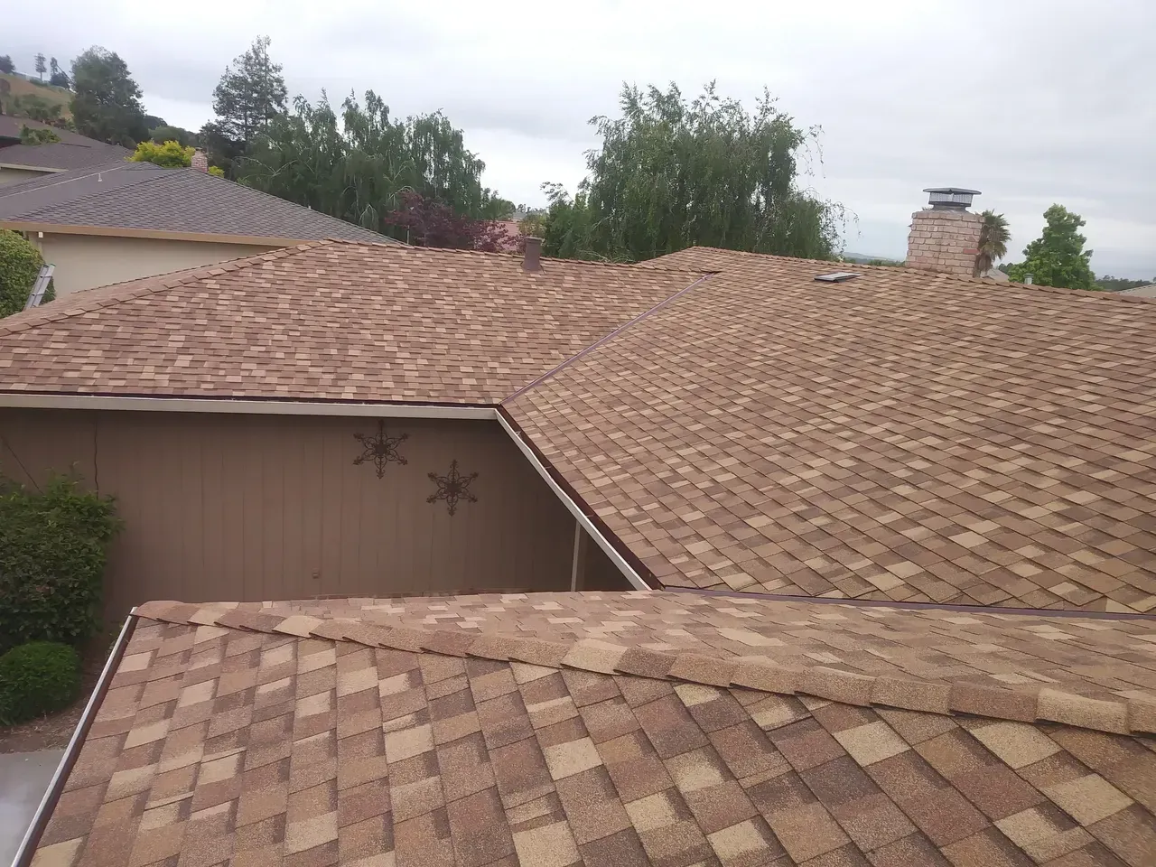 Brown shingle roofs of houses with a cloudy sky and trees in the background.