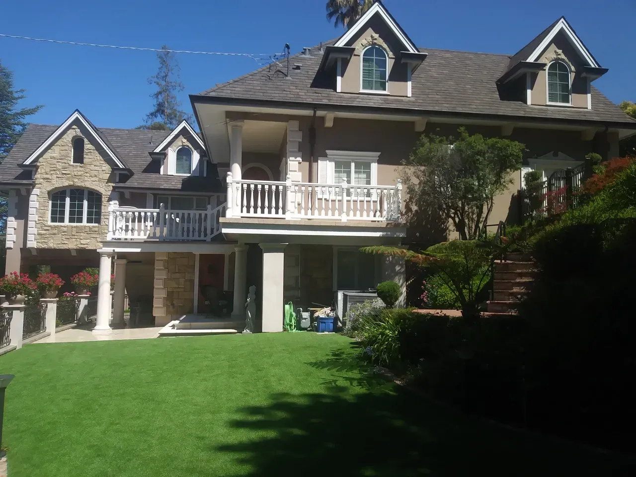 Large, multi-story house with stone and stucco facade, balcony, dormers, and green lawn.