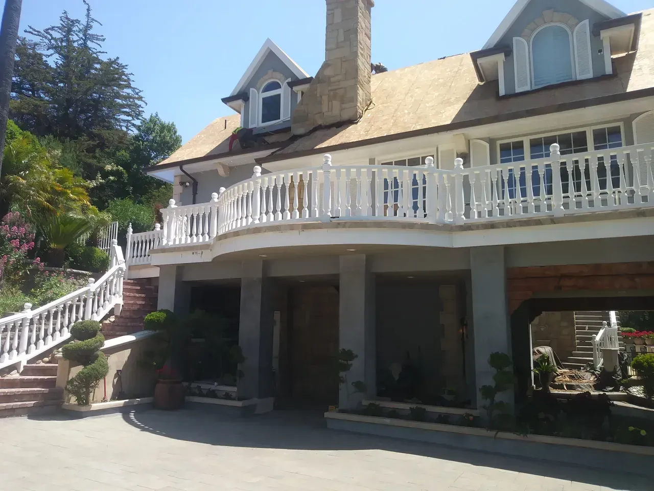 Two-story house with a white balcony, chimney, and landscaped stairs, under a bright blue sky.