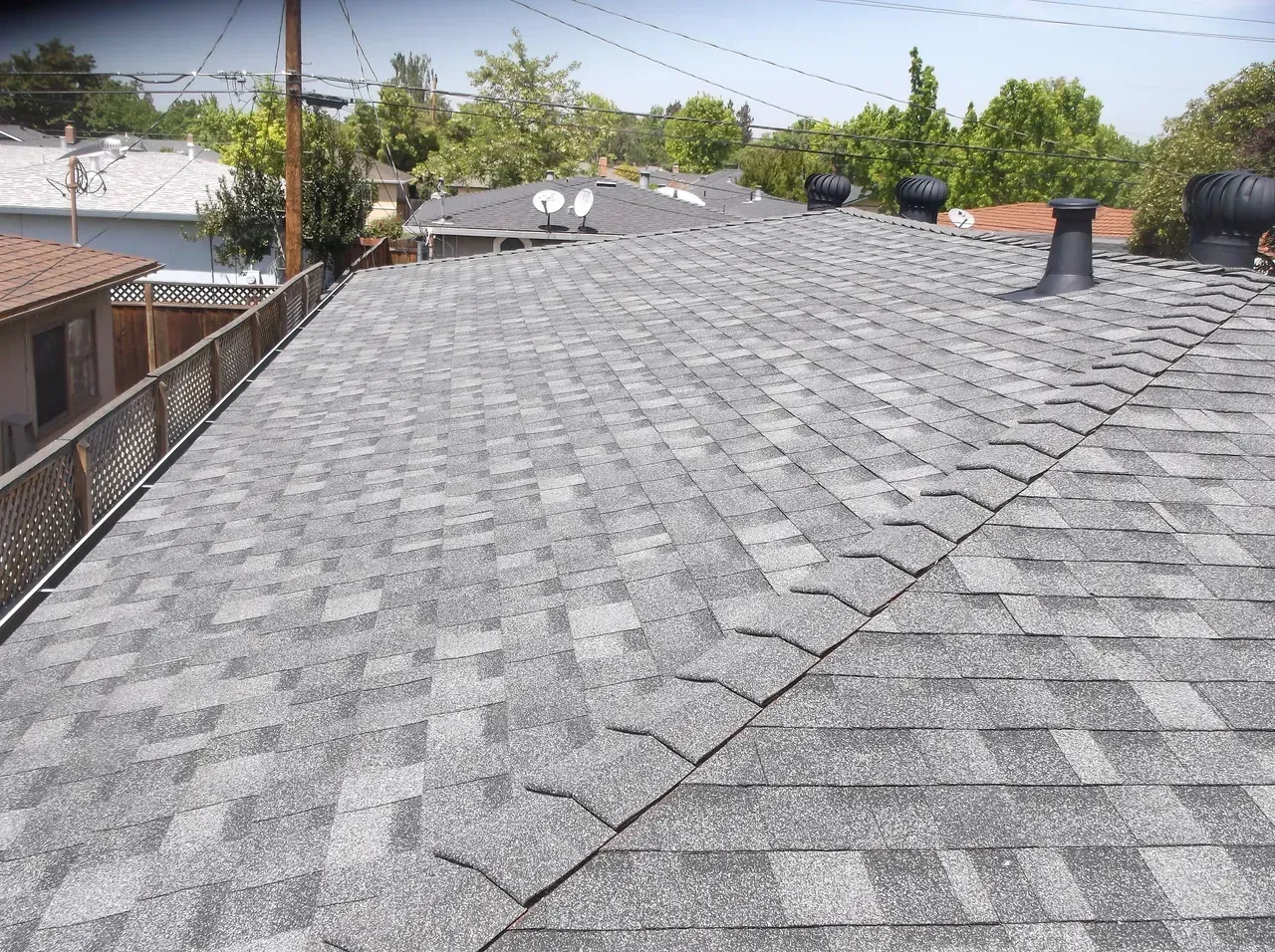 Gray asphalt shingle roof with vents, wooden fence, and trees in background.