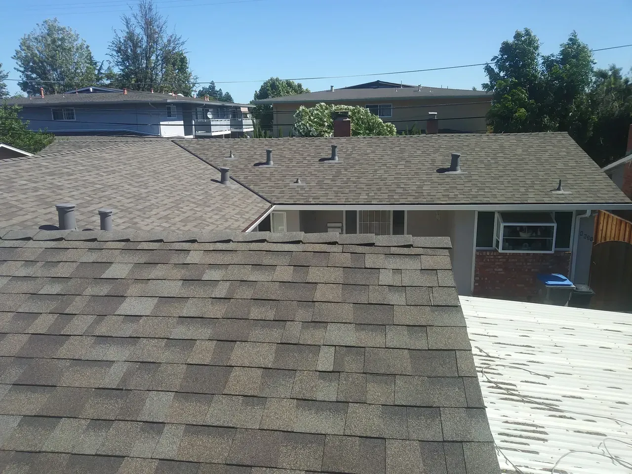 Roofs of houses, varying shades of brown, under a bright blue sky.