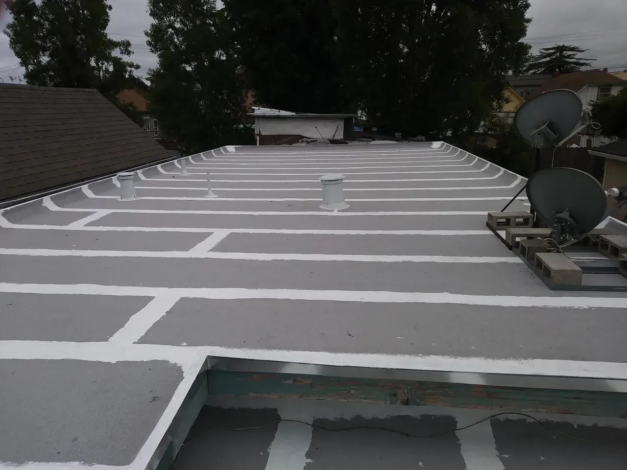 Flat roof with gray and white stripes, two satellite dishes, overcast sky.