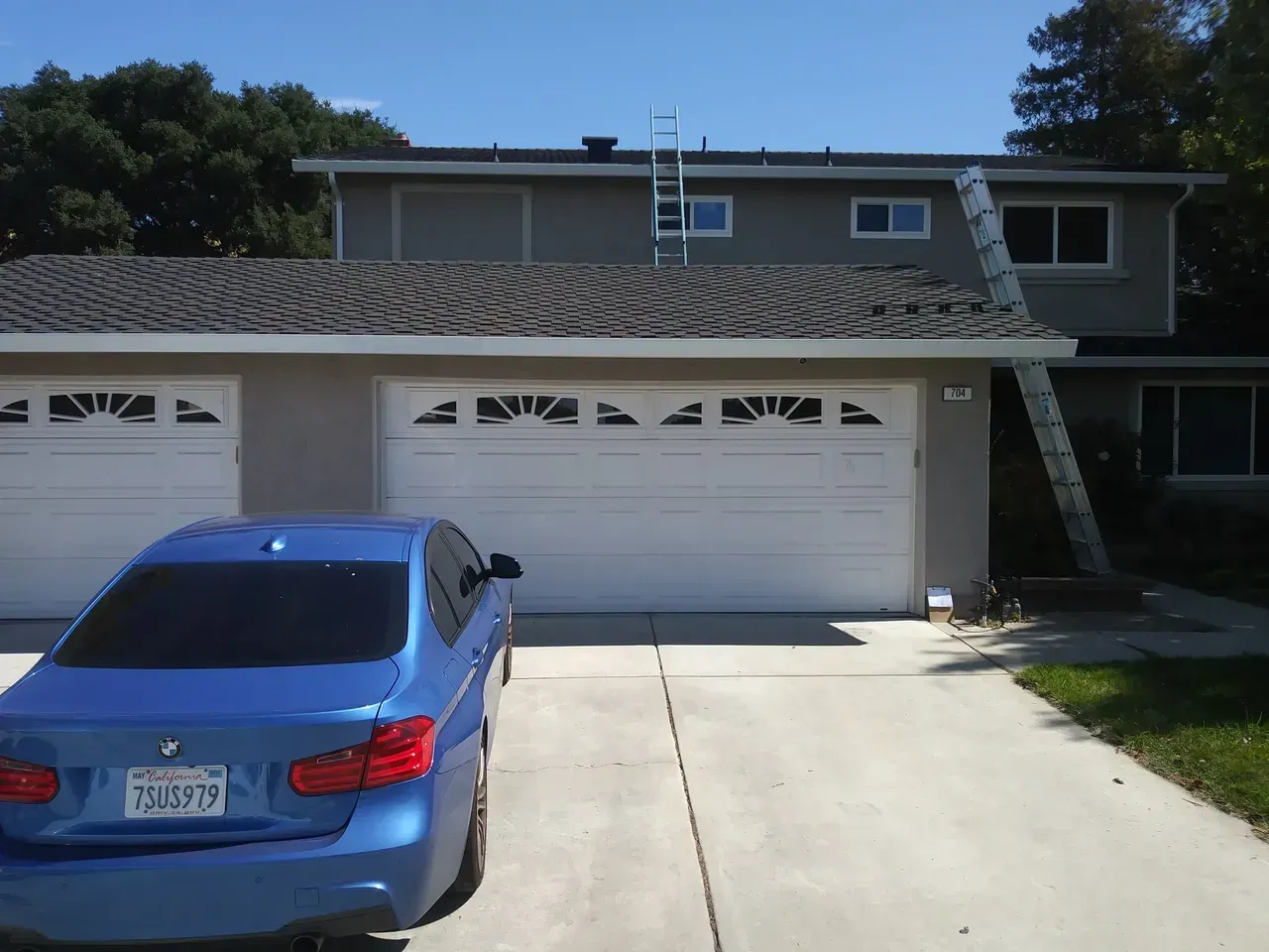 Blue car parked in front of a two-story house with a ladder leaning against it.