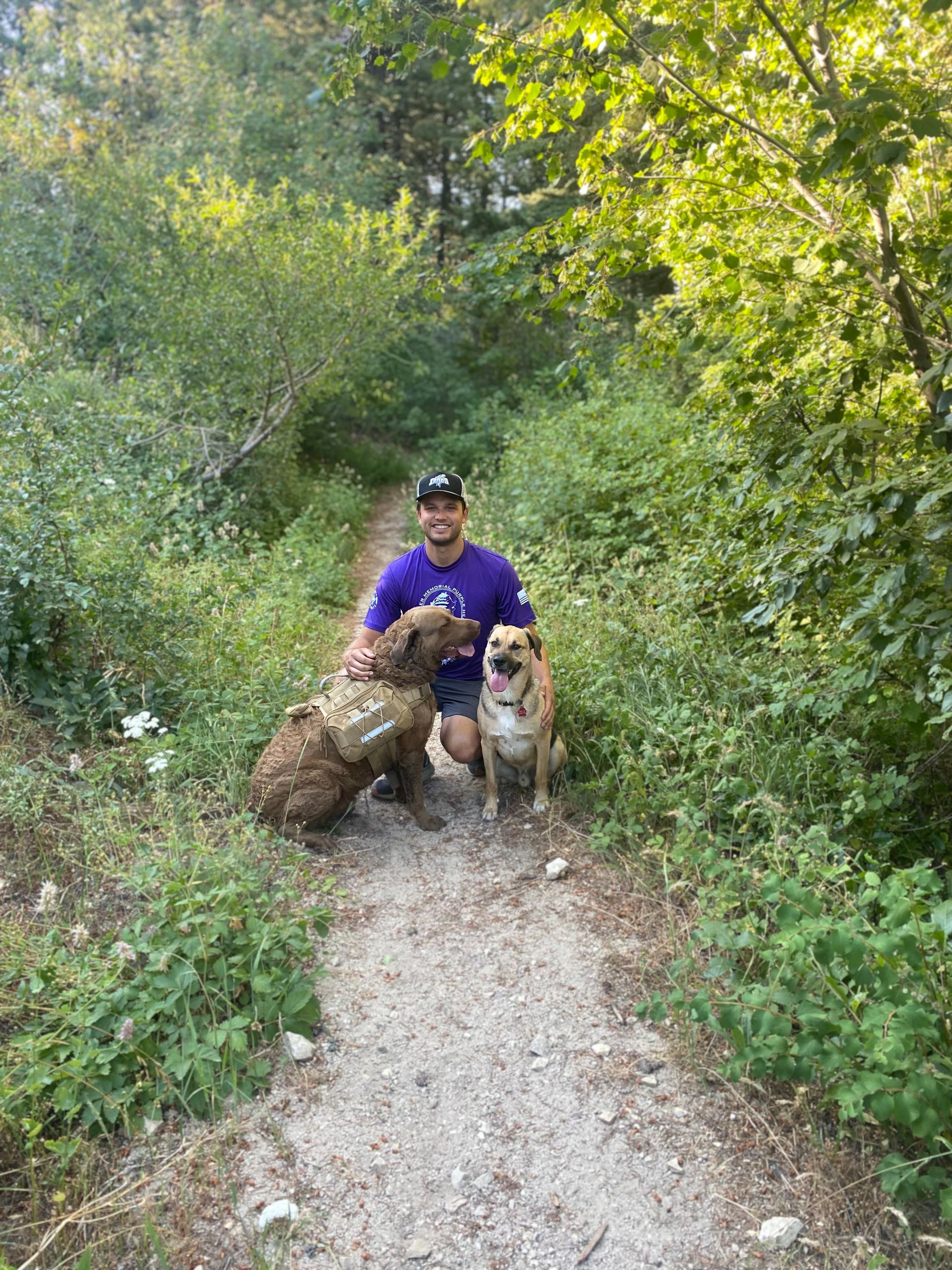 Man and two dogs on a rocky mountain, smiling in the sun.