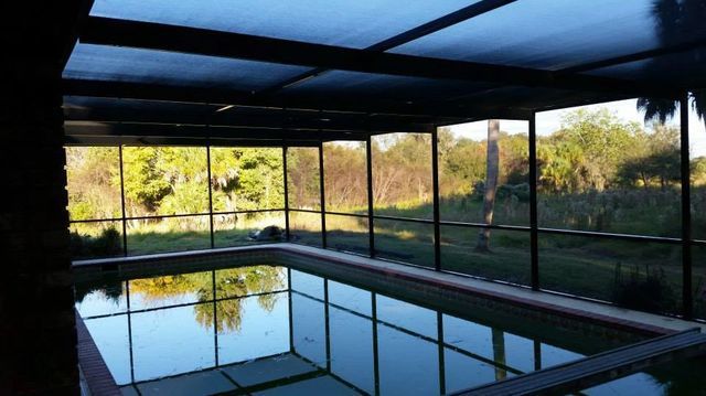 An indoor swimming pool with a screened in area and trees in the background