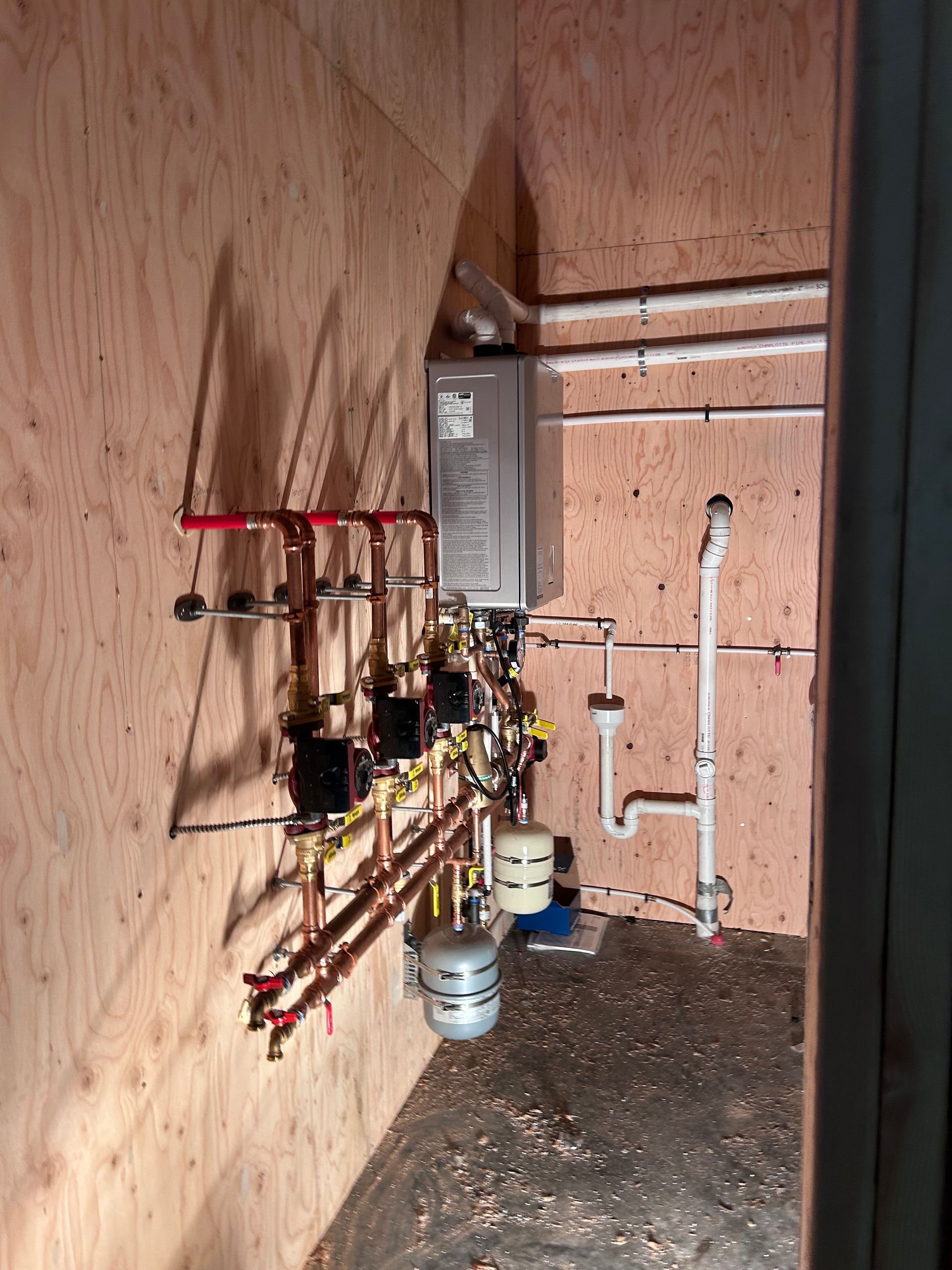 Heating system installed on a wood wall, including pipes, valves, a water heater, and expansion tank.