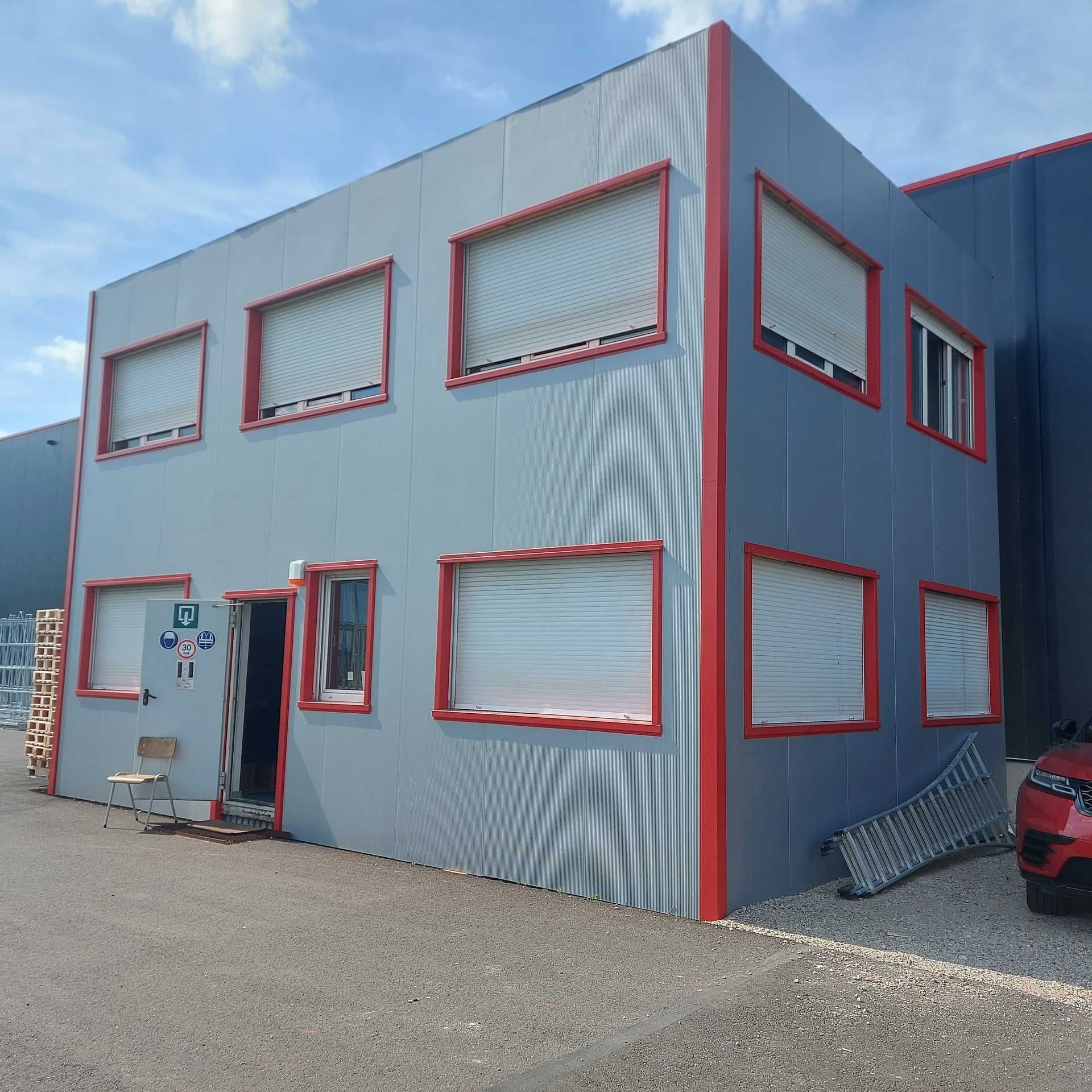 Een grijs gebouw met rode randen en een bordje met daarop 'a'