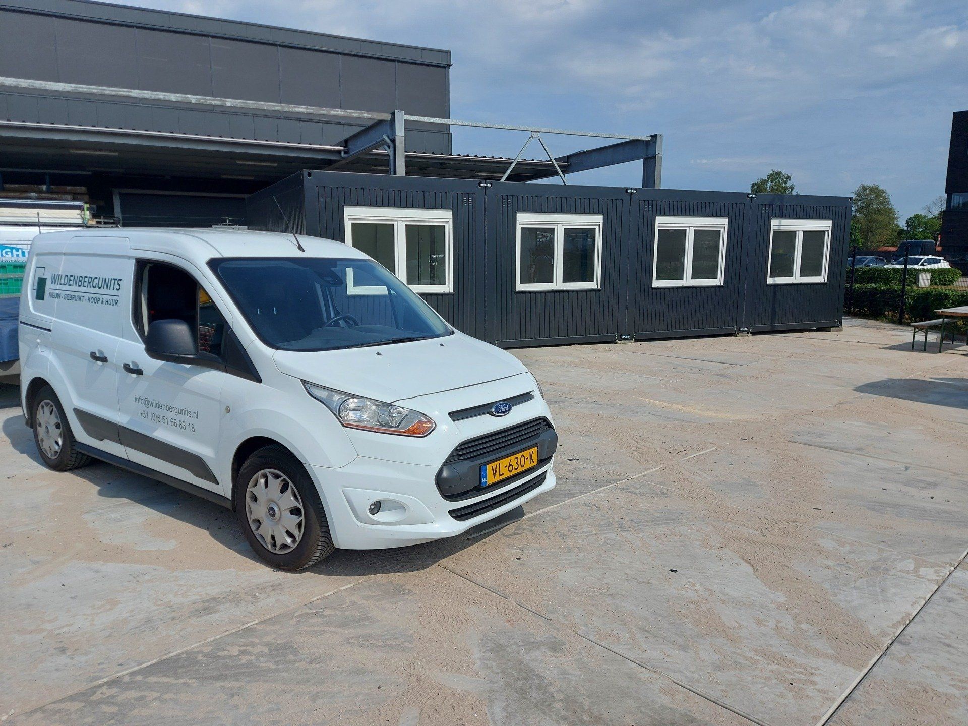 Een wit busje staat geparkeerd op een parkeerplaats voor een gebouw.