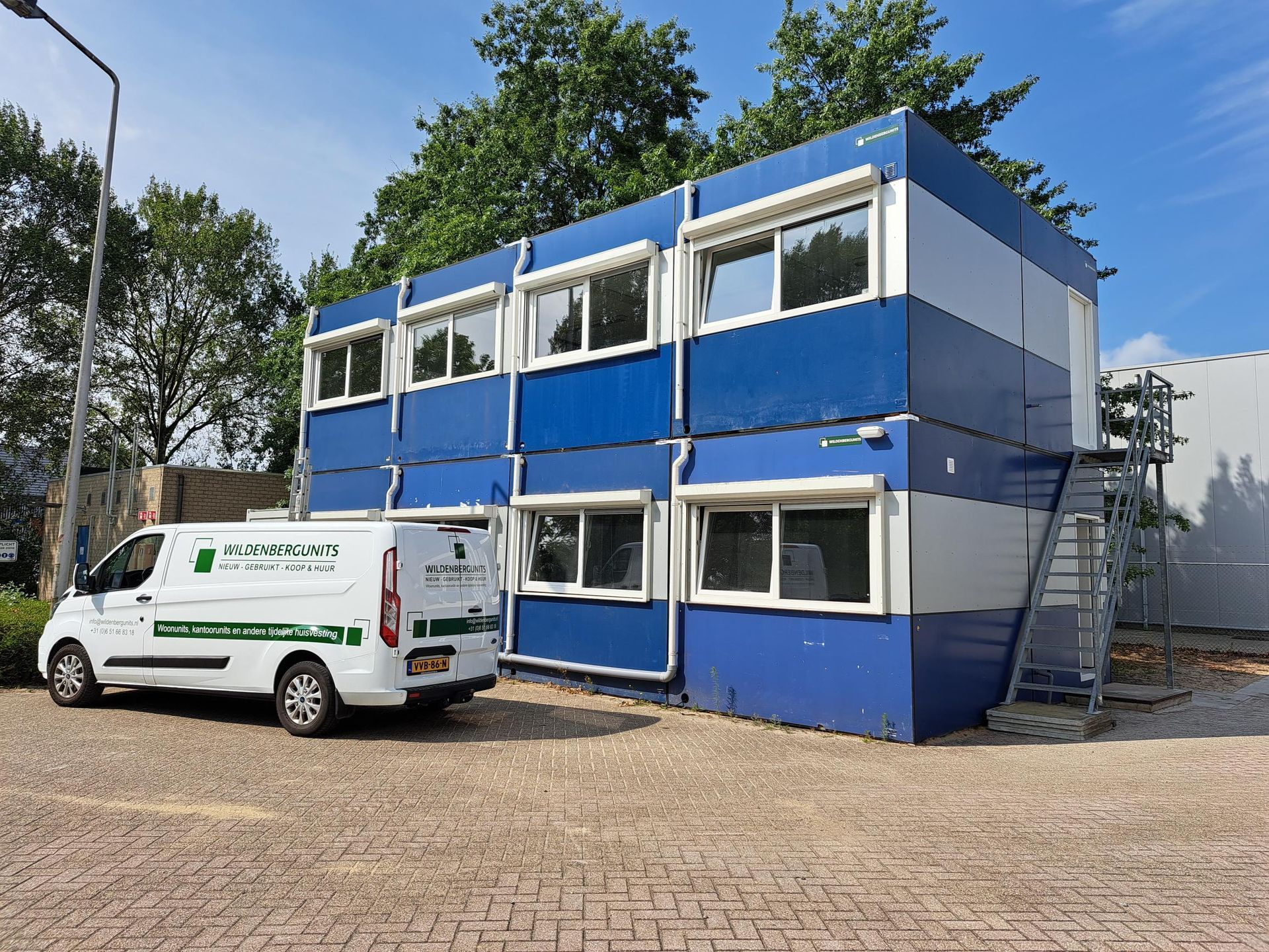 Een wit busje staat geparkeerd voor een blauw-wit gebouw.