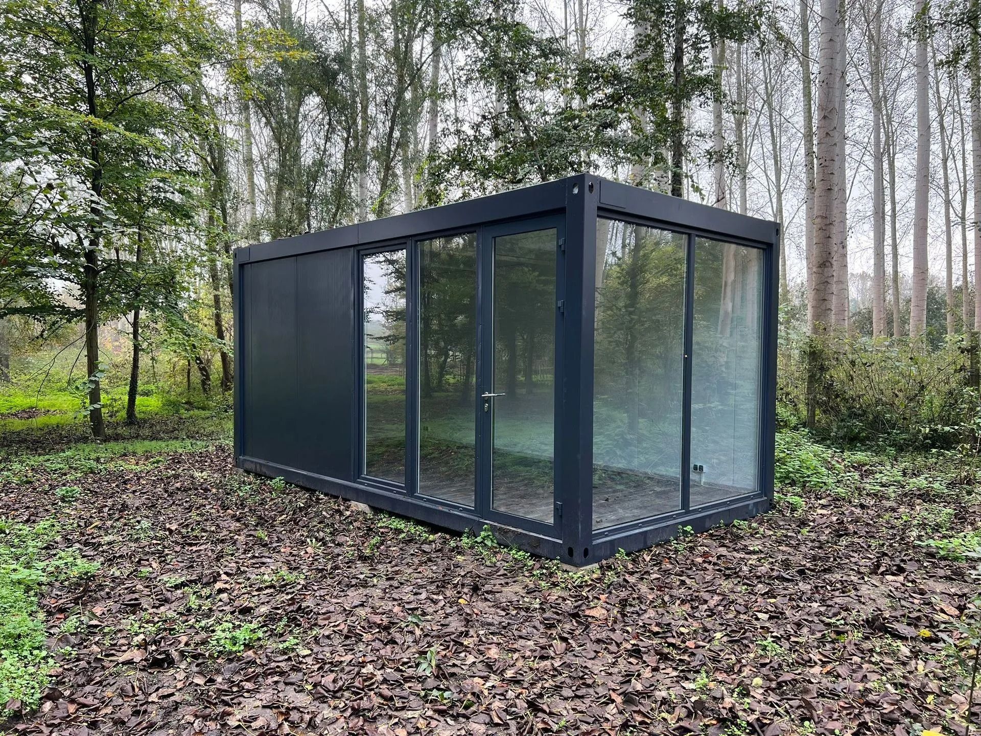 Een klein gebouw met veel ramen staat midden in een bos.
