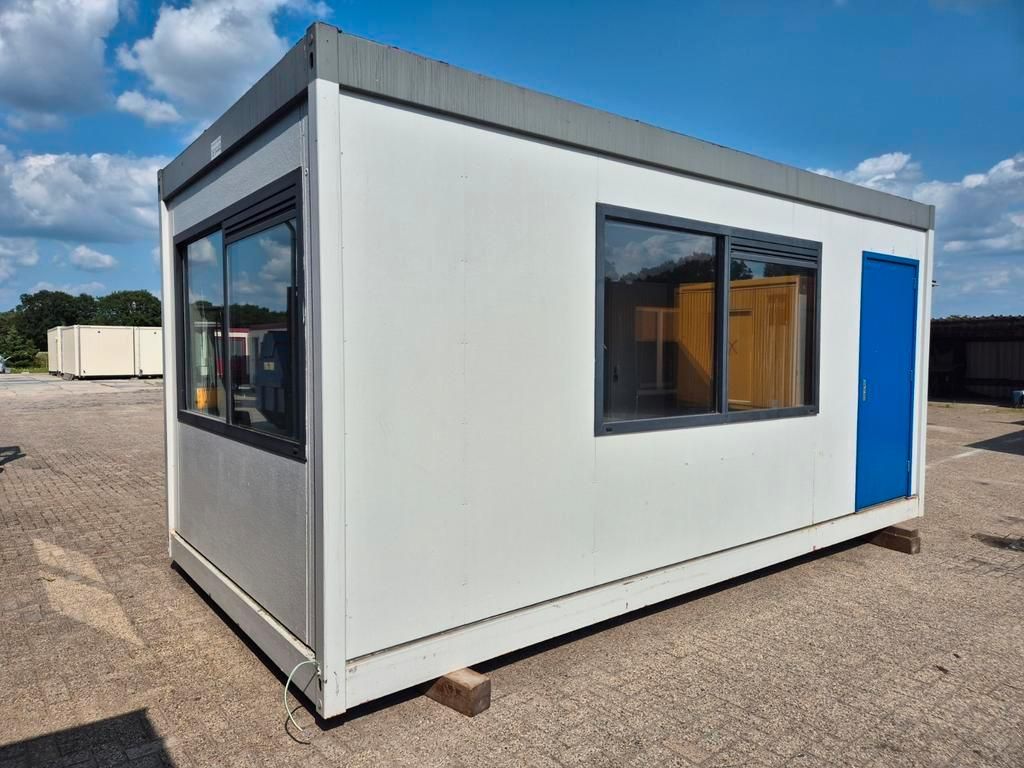 Een klein wit gebouw met een blauwe deur en ramen staat op een veld van zand.