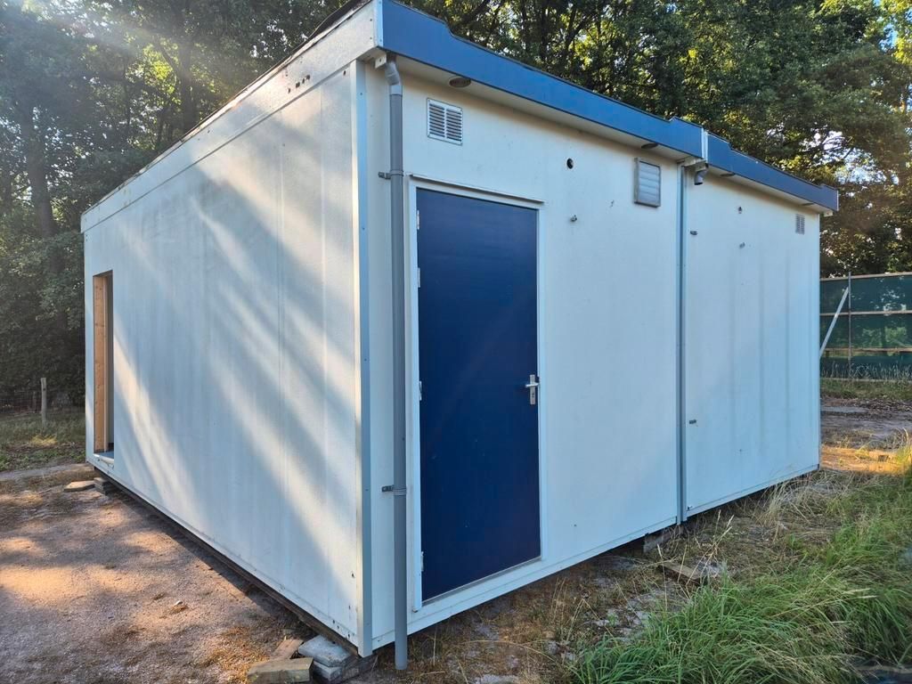Een wit gebouw met een blauwe deur staat in het gras.