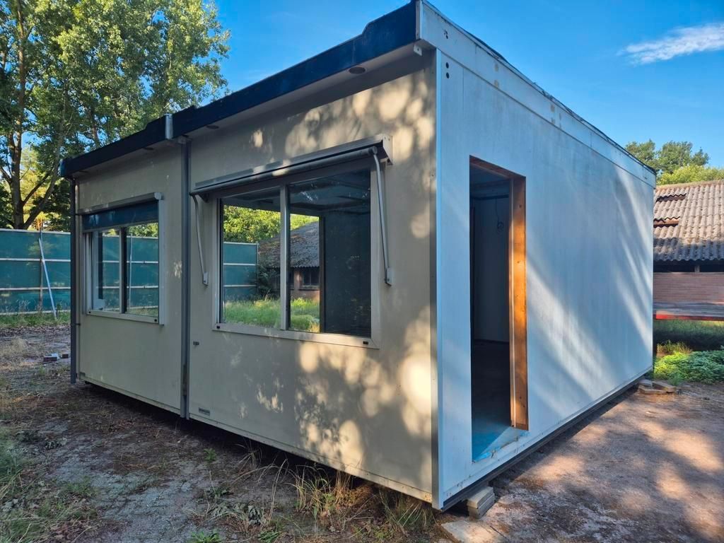 Een klein wit gebouw met een deur en ramen staat op een veld van zand.