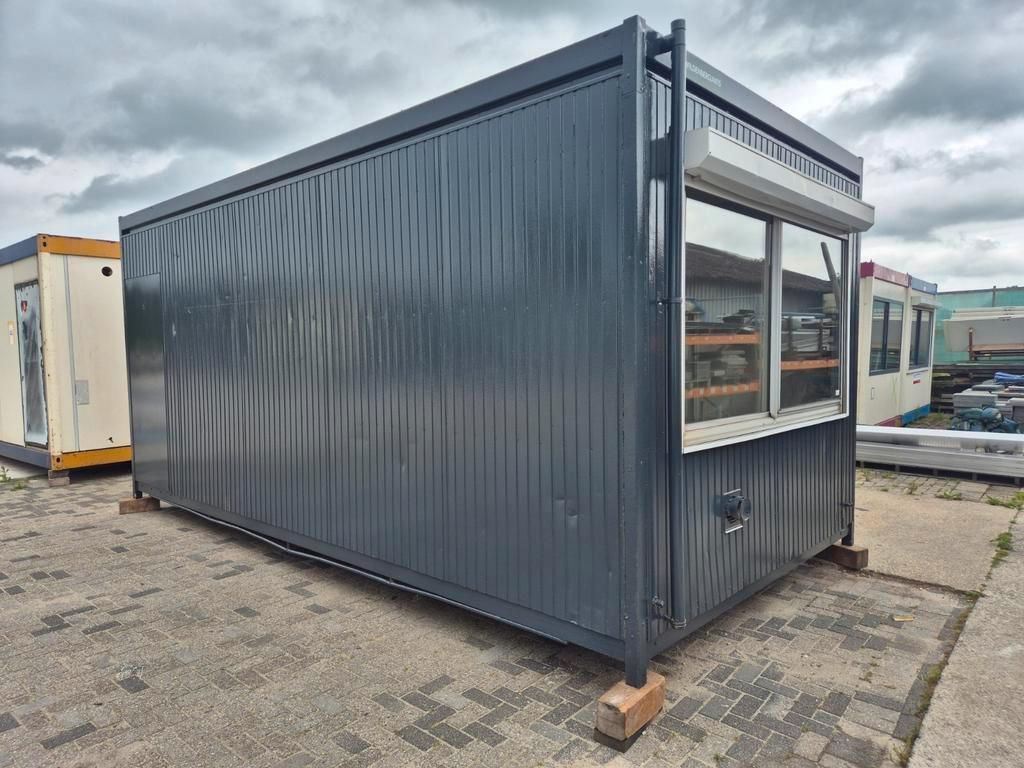 Een grijze container staat op een bakstenen stoep op een parkeerplaats.