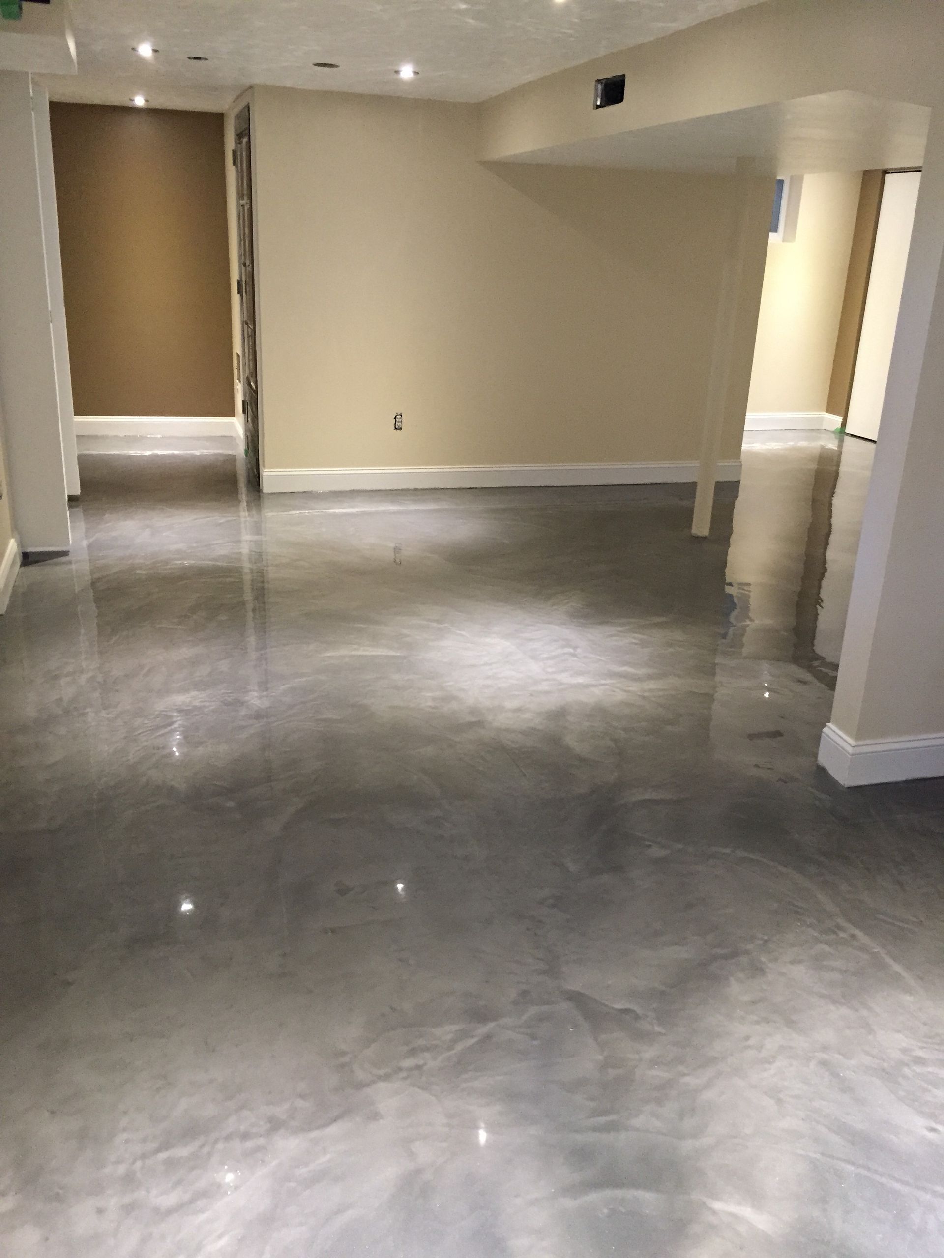 A room with a polished, metallic gray epoxy floor reflecting overhead lights, surrounded by light tan walls.