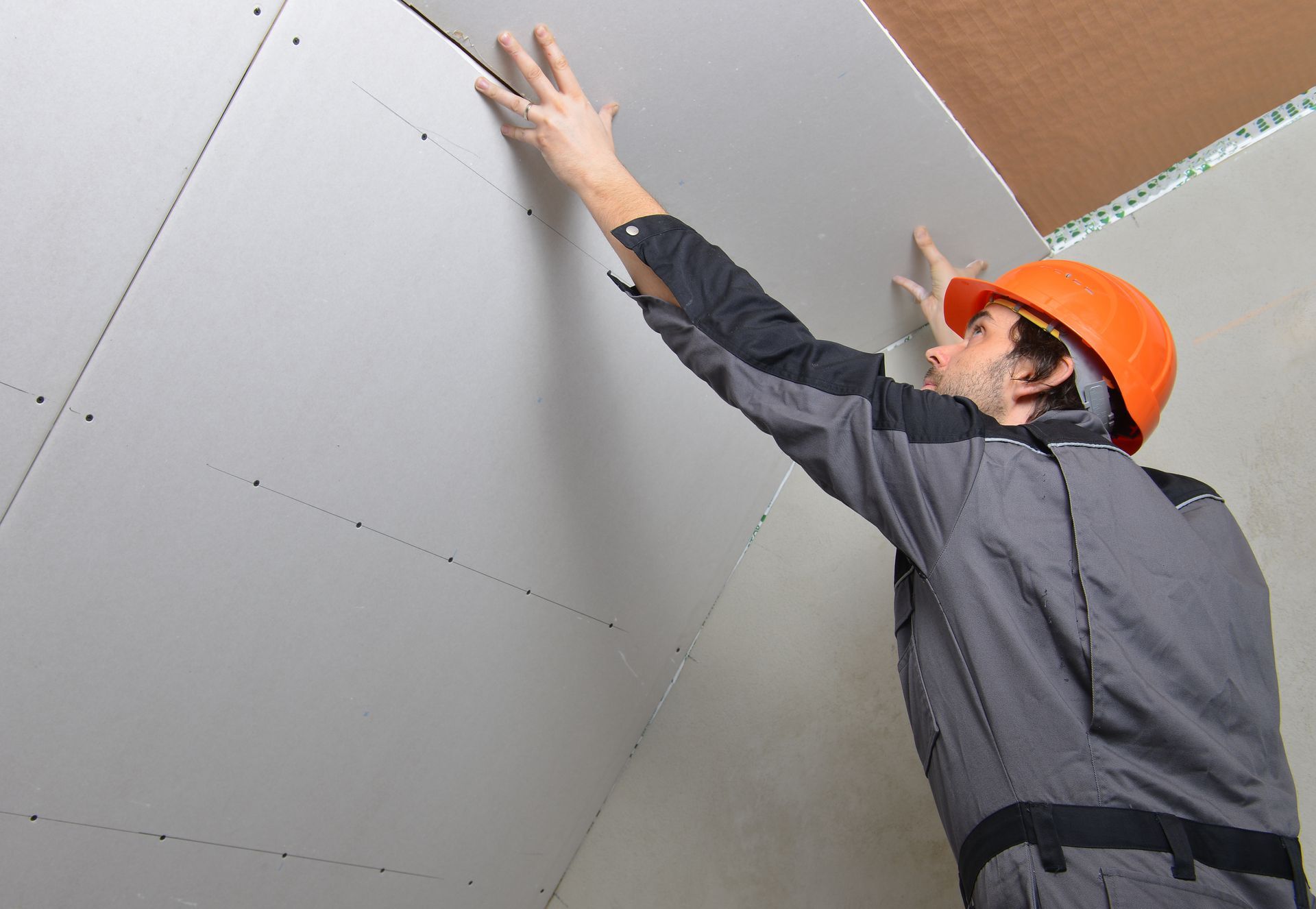 A man wearing a hard hat is working on a wall.