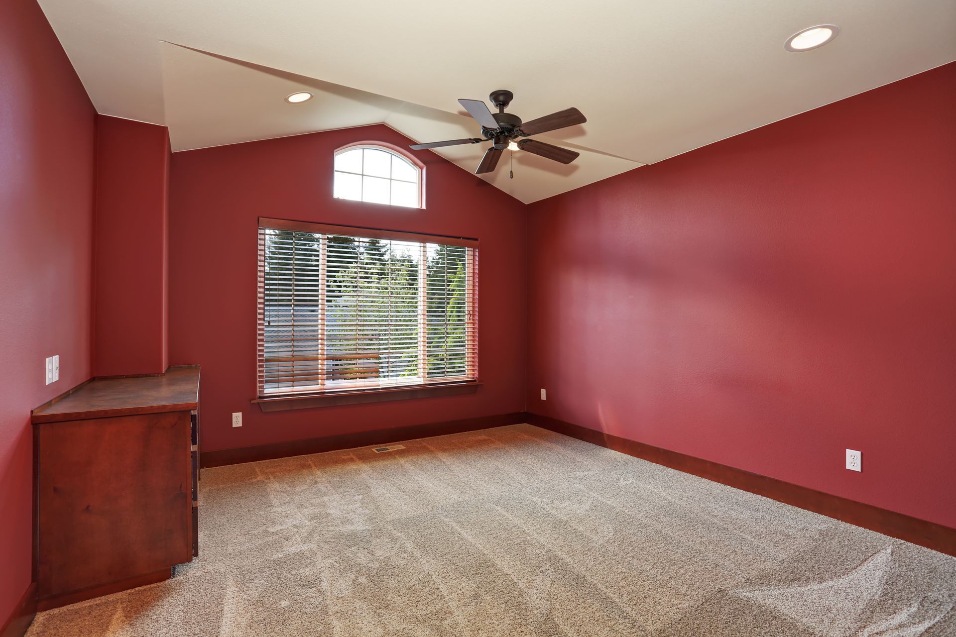 An empty bedroom with red walls and a ceiling fan