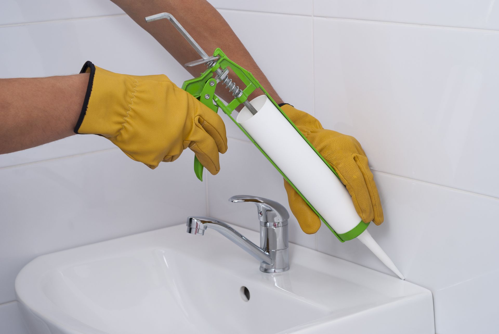 A person is applying caulk to a bathroom sink.