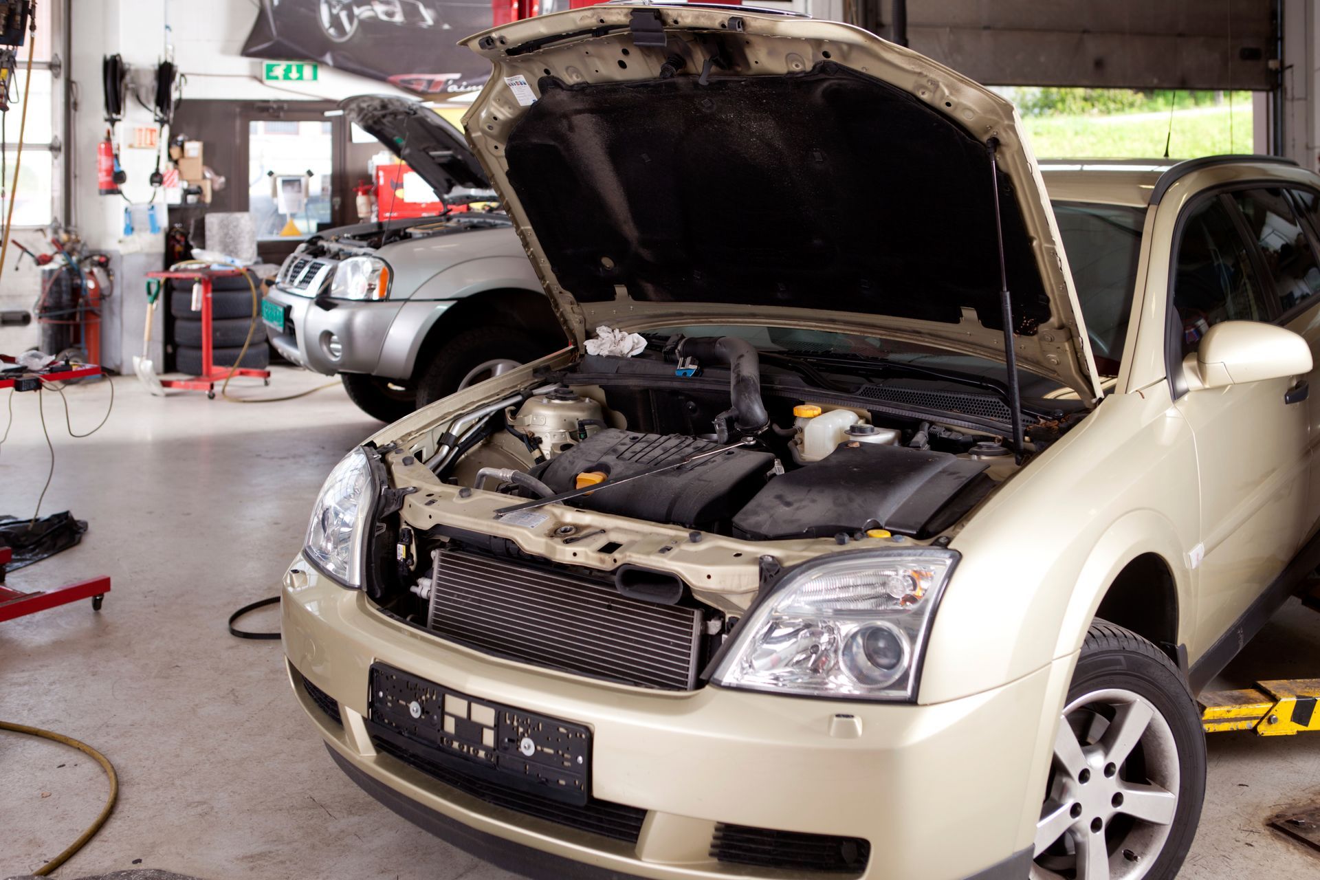 Car with open hood in auto repair workshop, engine bay exposed for maintenance and diagnostics tasks.