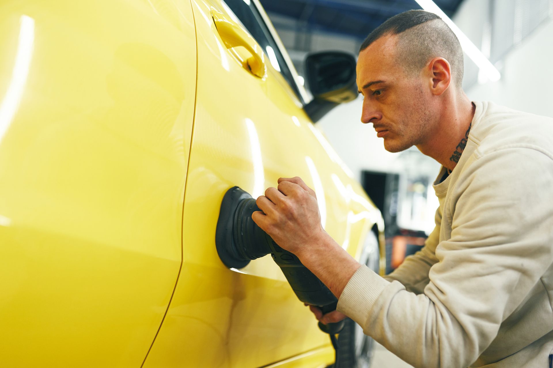 Man polishing a yellow car using a professional tool. Man polishing a yellow car using a professional tool.