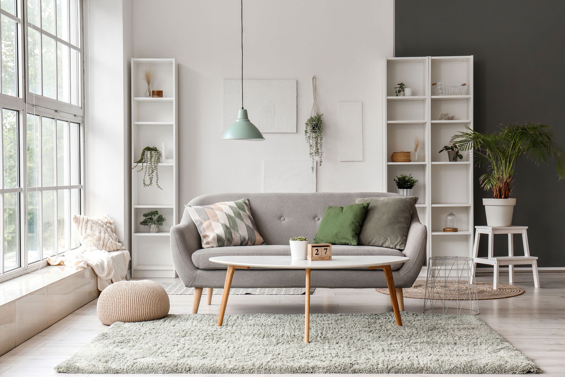 Living room with gray sofa, white shelves, rug, and large window.