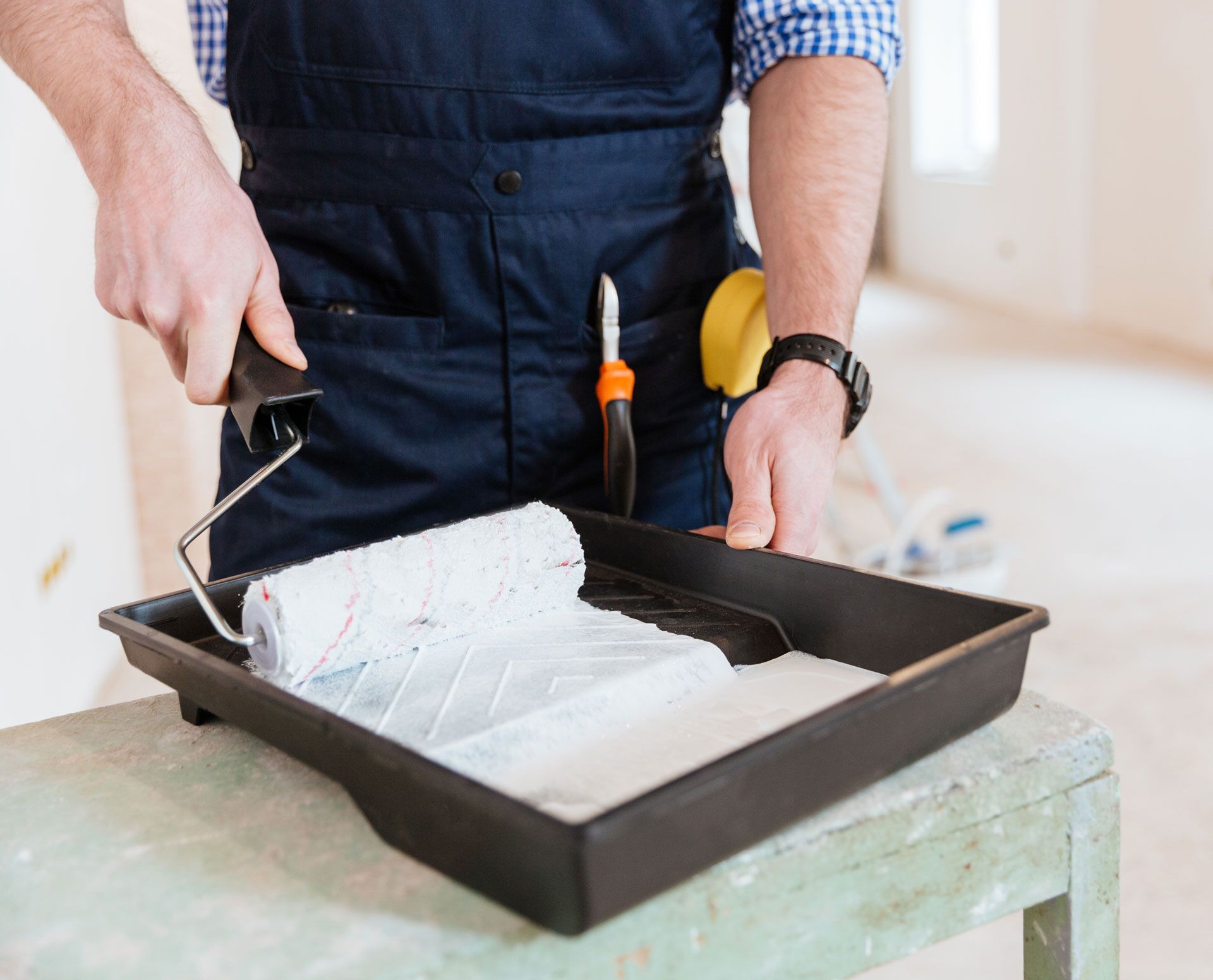 Person using a paint roller in a tray with white paint.